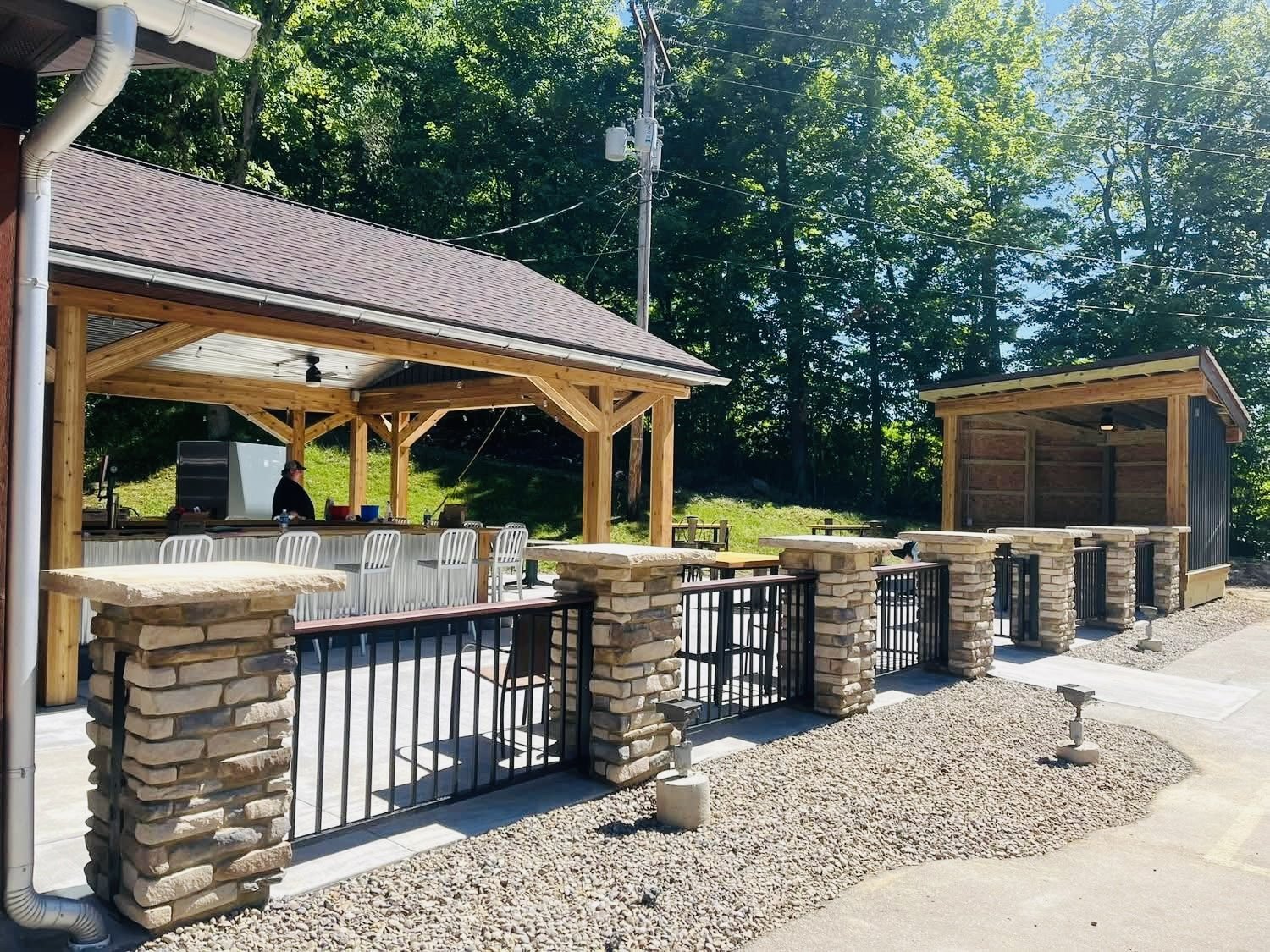 Covered wood outdoor pavilion with stone-pillar patio wall and black railing, built by Warrior Barriers in Tuscarawas County, Ohio